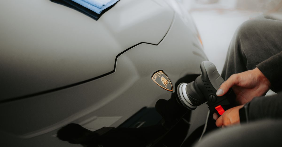 A detailer buffing a car panel with a machine polisher in a dark studio